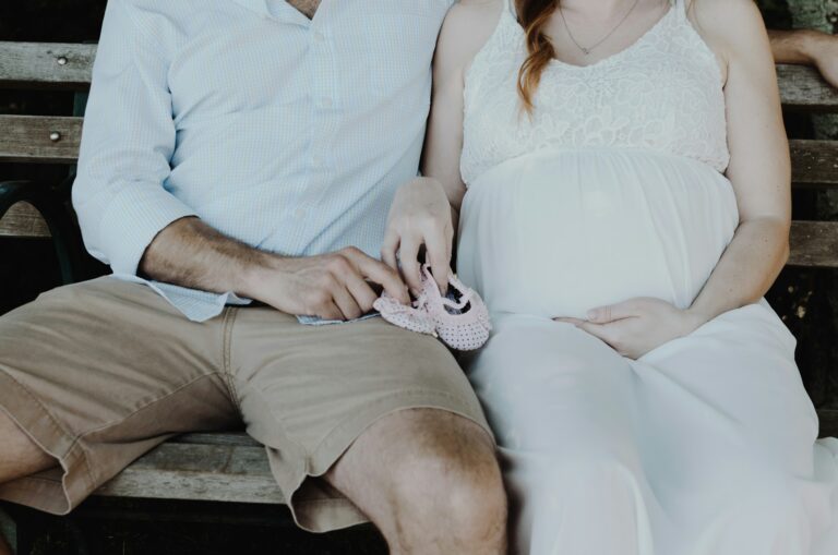 A pregnant couple sitting together on a bench