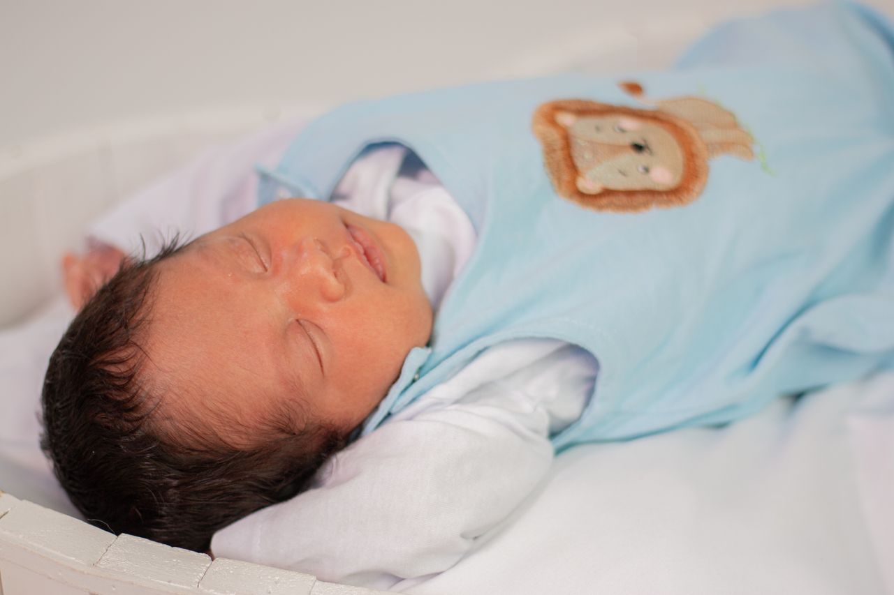 A serene newborn baby sleeps peacefully in a light blue outfit with animal designs.